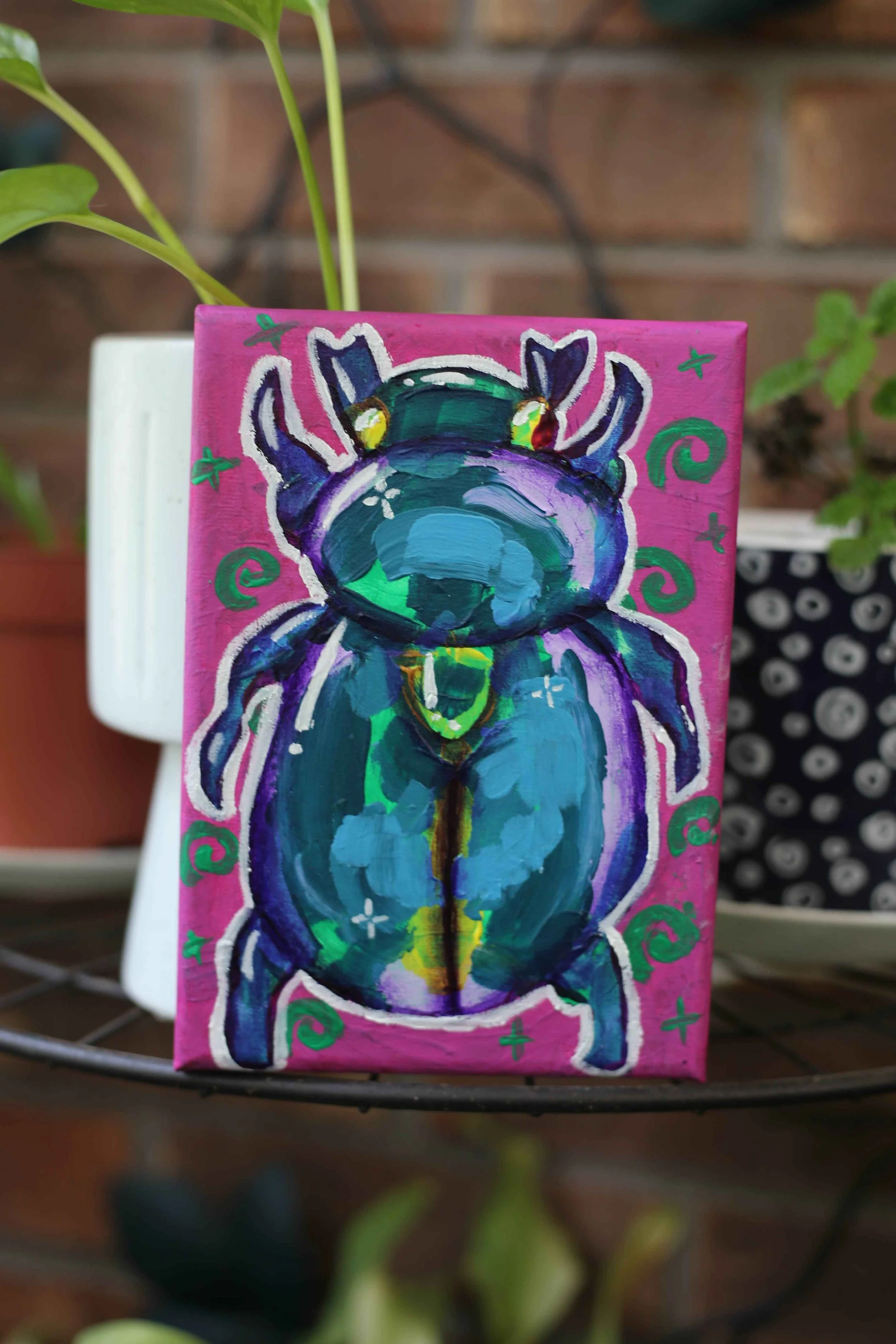 A vibrant painting of a teal and purple beetle on a hot-pink canvas, created by an Art Inclusive artist