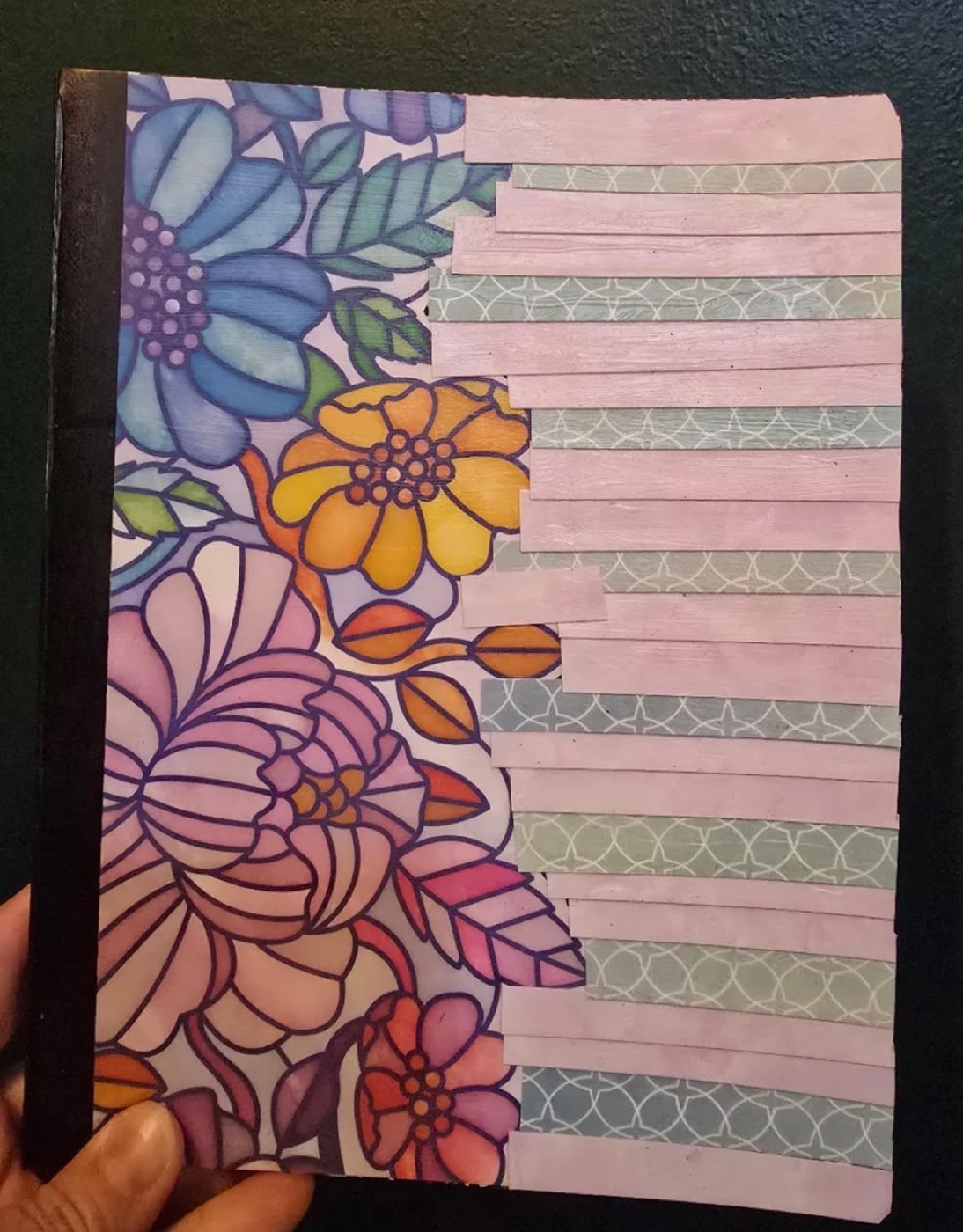 A decoupaged notebook cover with floral art and strips of pink and grey tissue paper.